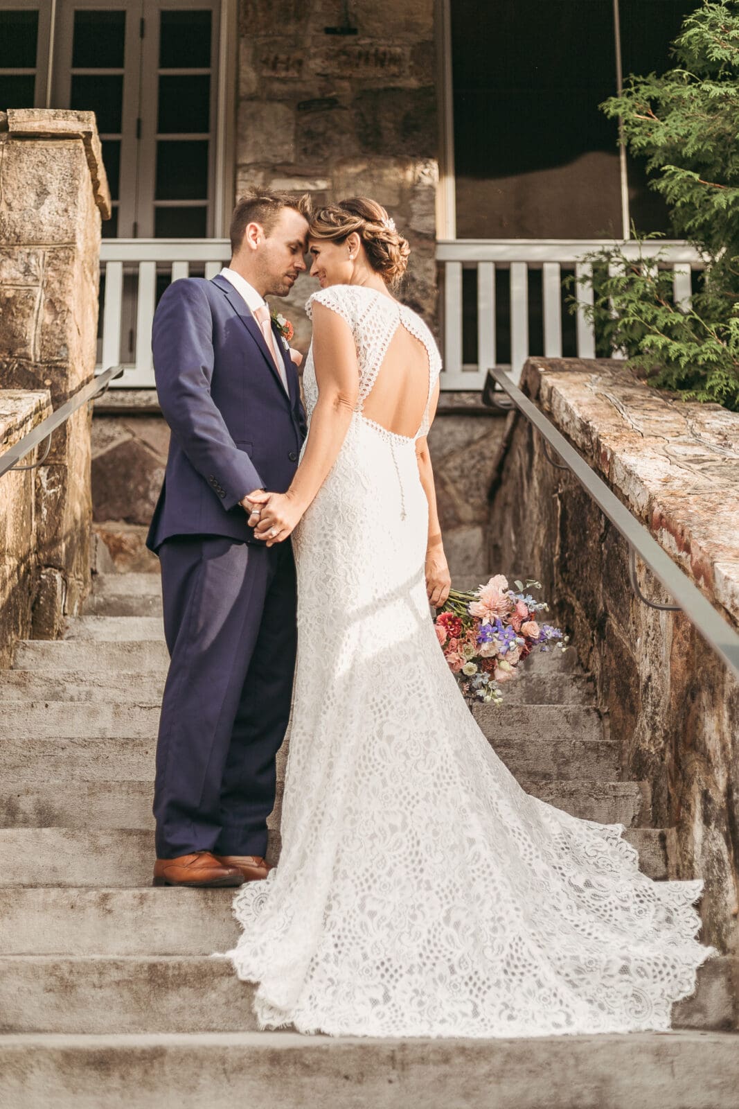 Bride and groom standing on stone stairs with wedding dress spread out showing off the design.