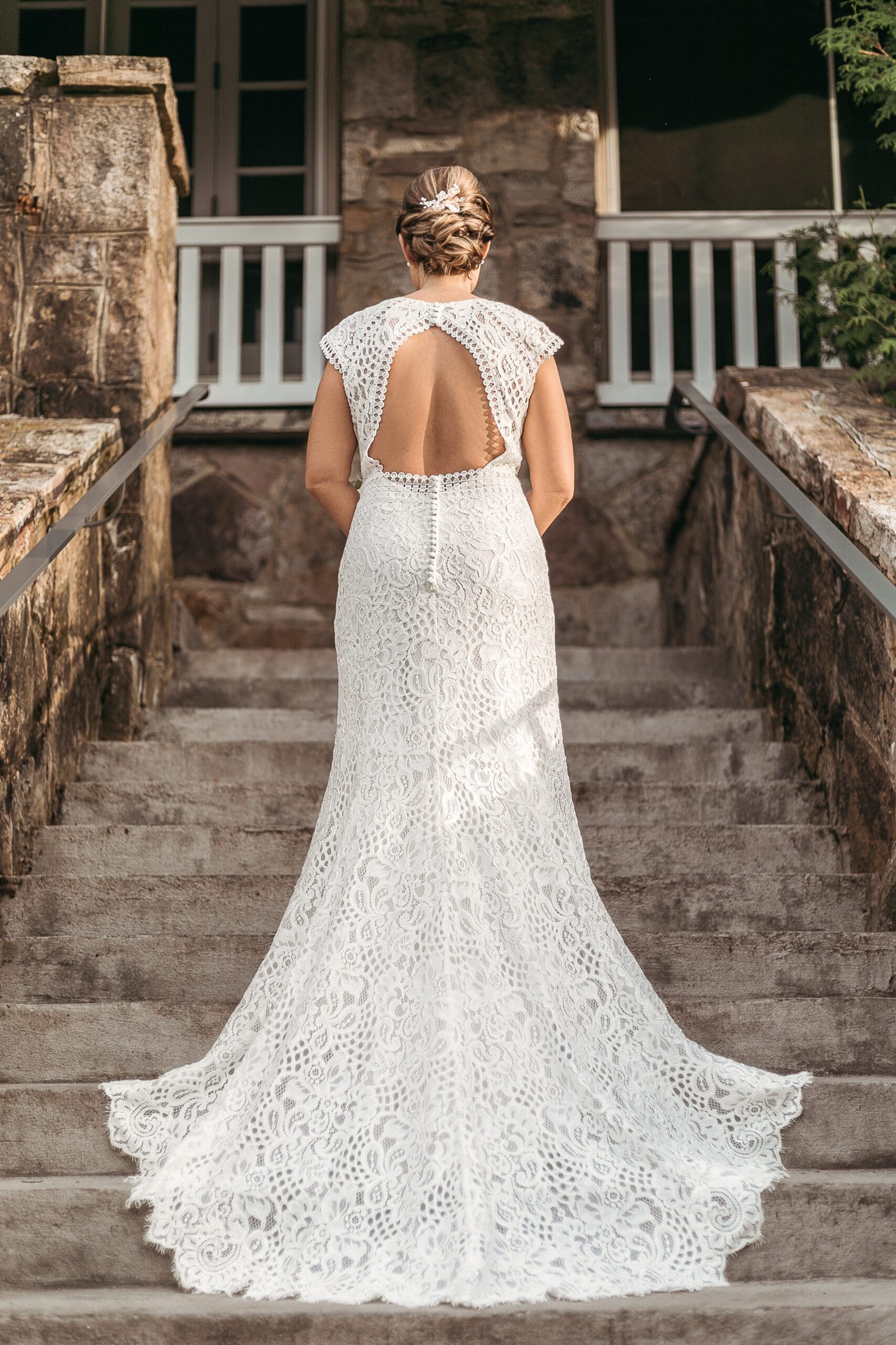Bride standing on stone stairs with wedding dress spread out showing off the design.