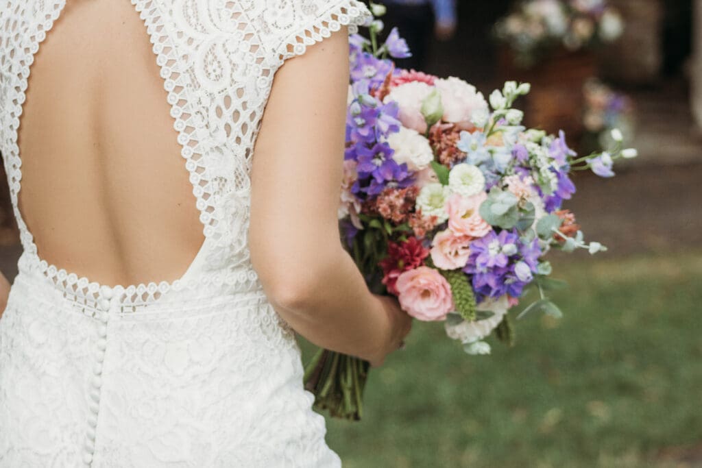 Bride at elopement standing in front of woods smiling big while holding her bouquet.