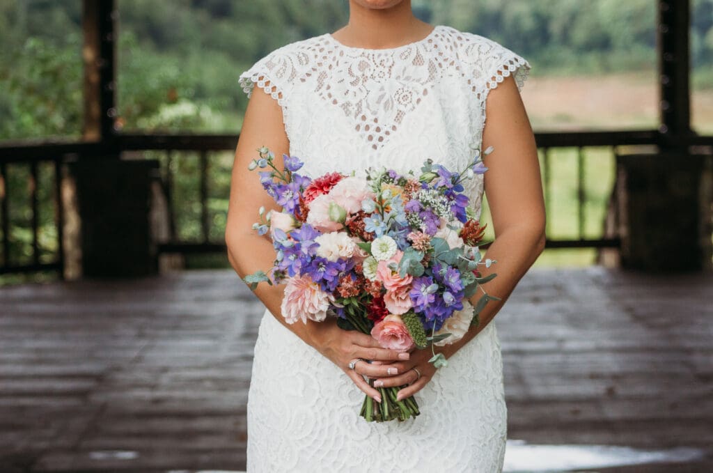 Bride at elopement standing in front of woods smiling big while holding her bouquet.