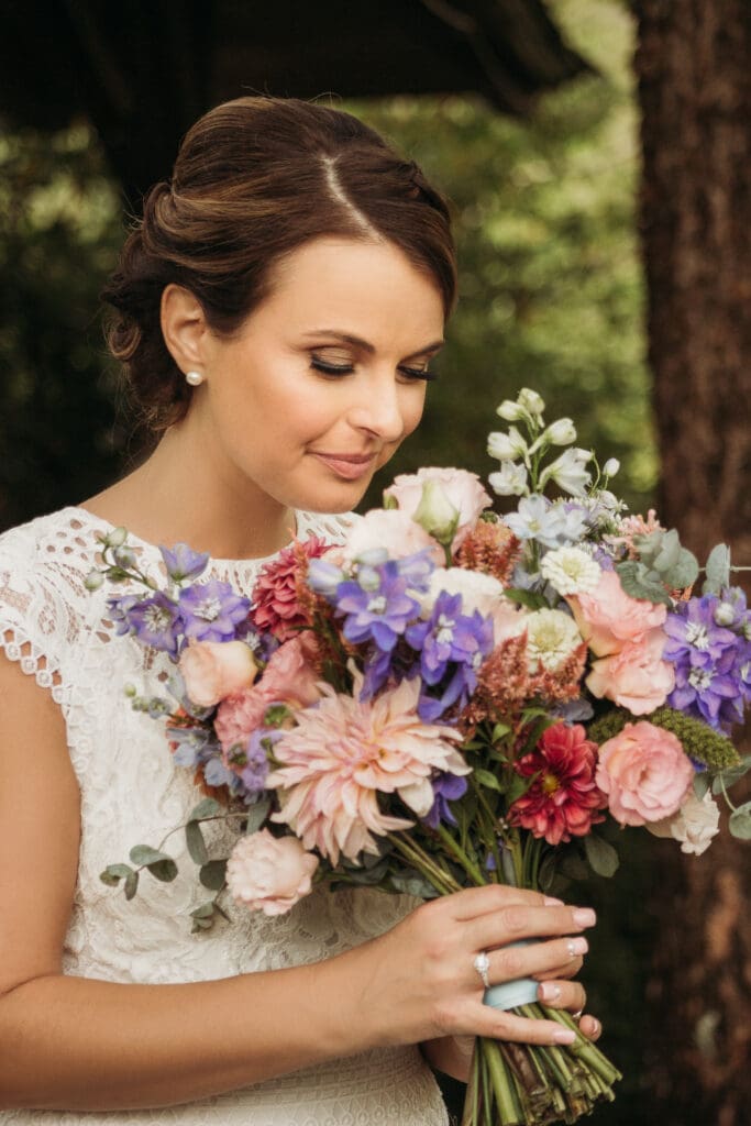 Bride at elopement standing in the woods smelling her bouquet of fresh flowers.