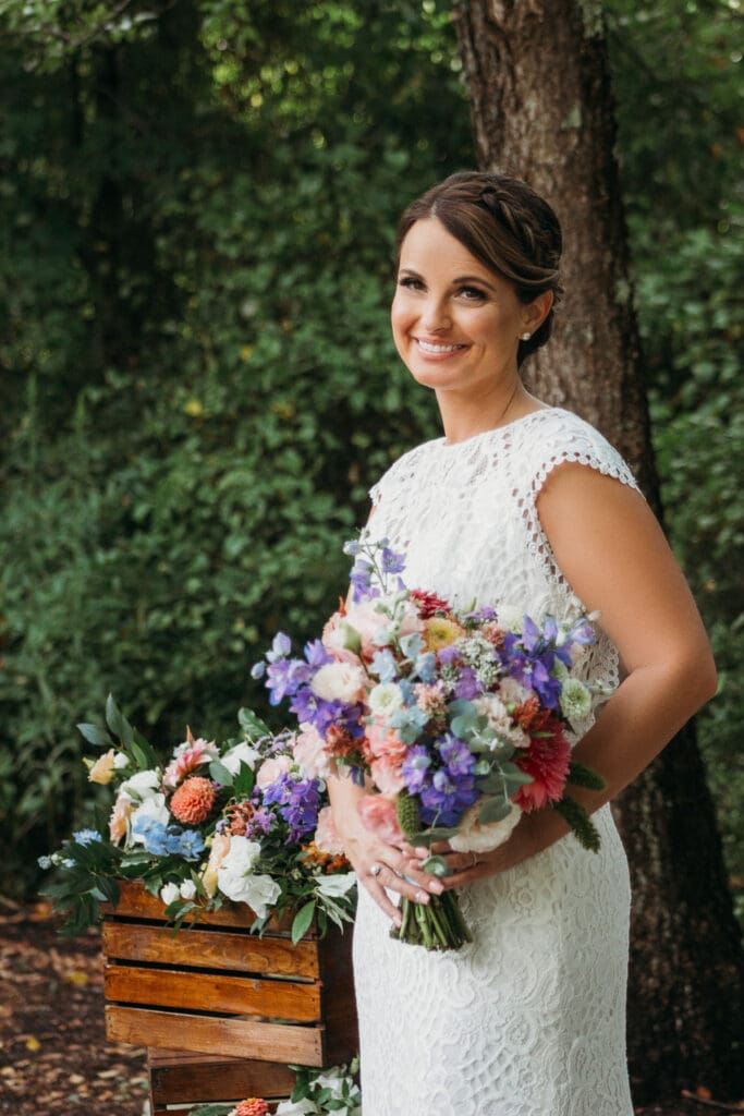 Bride at elopement standing in front of woods smiling big while holding her bouquet.