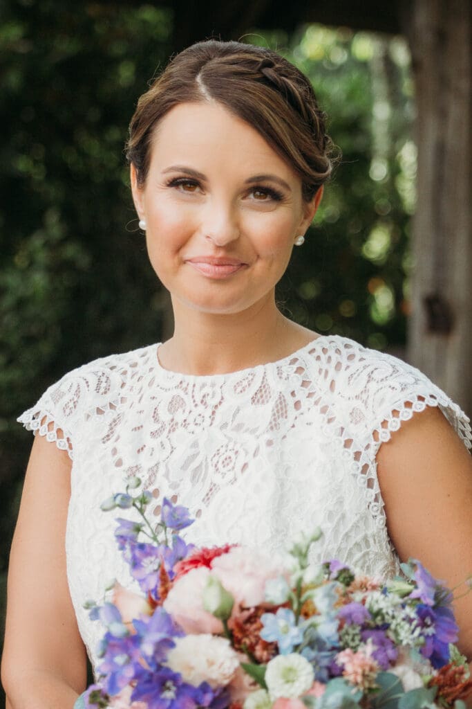 Bride at elopement standing in front of woods smiling big while holding her bouquet.