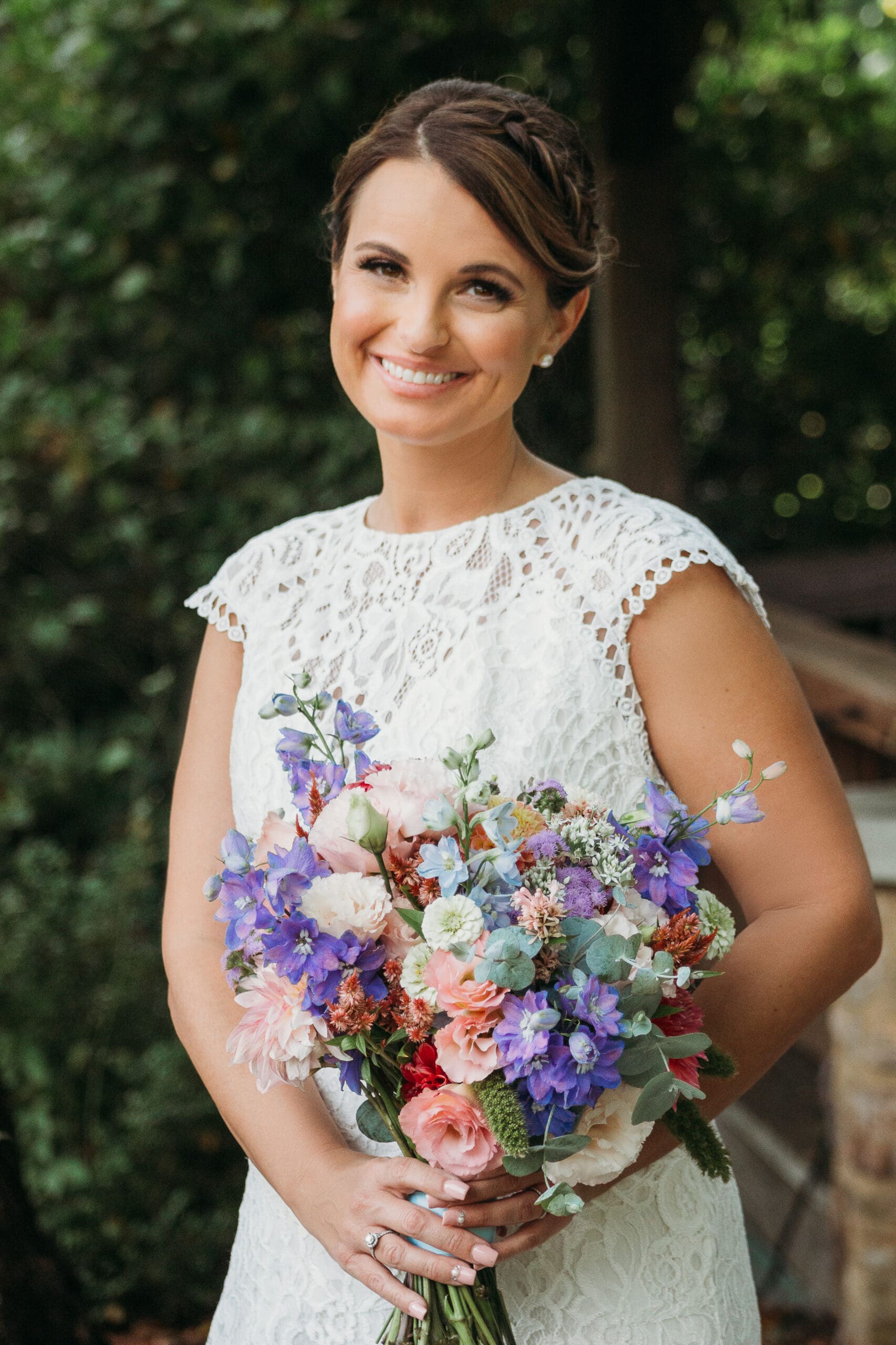Bride at elopement standing in front of woods smiling big while holding her bouquet.
