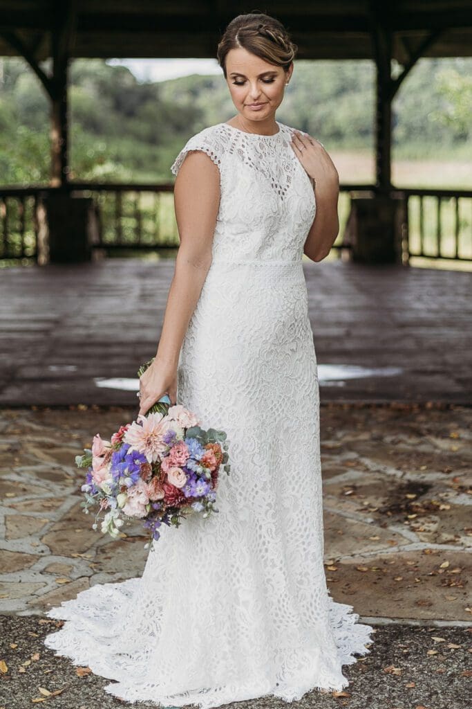 Bride at elopement standing in front of woods smiling big while holding her bouquet.