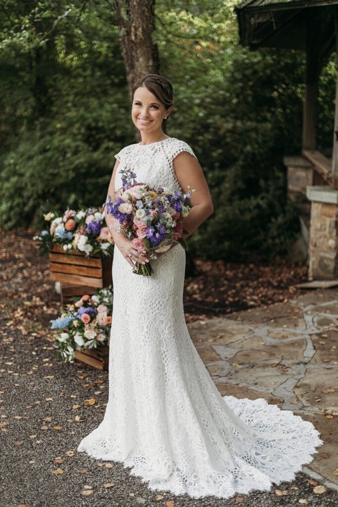 Bride at elopement standing in front of woods smiling big while holding her bouquet.