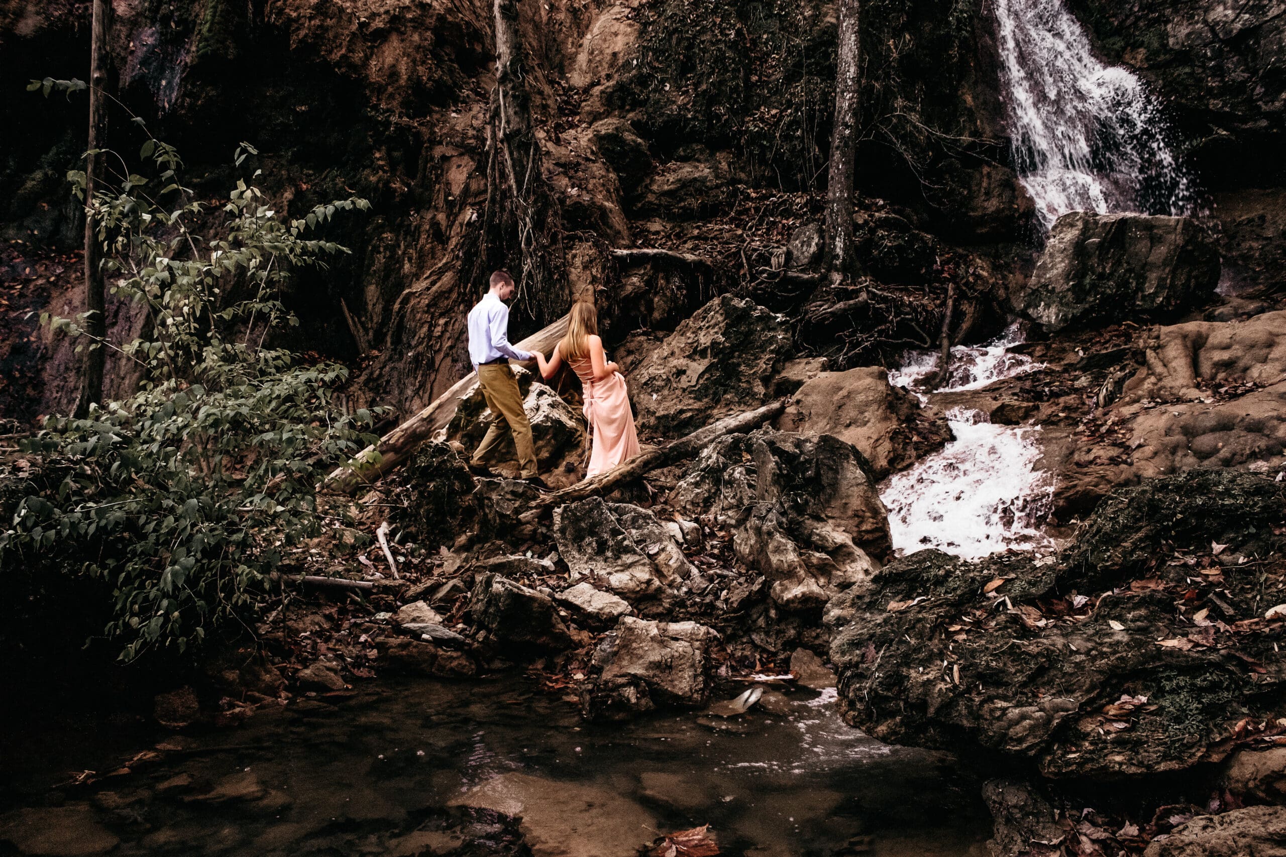 Couple standing in front of a waterfall in winter with their wedding attire on a few spots of greenery popping out in a sea of brown. They used me to plan their waterfall elopement
