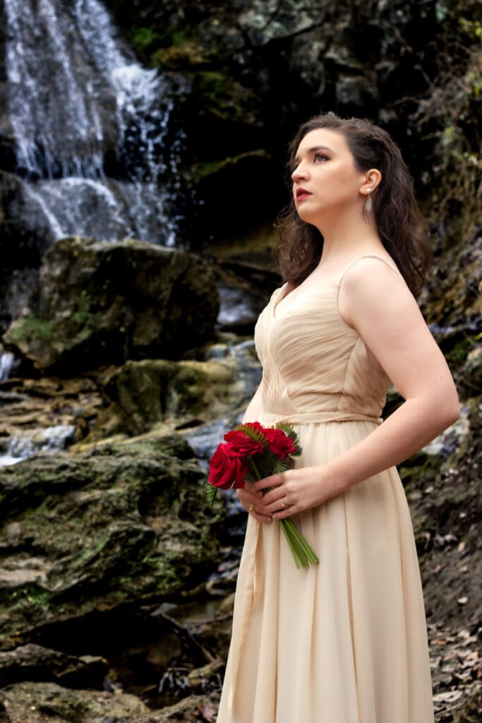 Couple standing in front of a waterfall in winter with their wedding attire on a few spots of greenery popping out in a sea of brown.