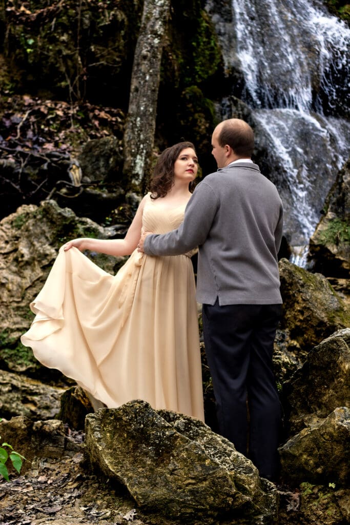 Couple standing in front of a waterfall in winter with their wedding attire on a few spots of greenery popping out in a sea of brown.