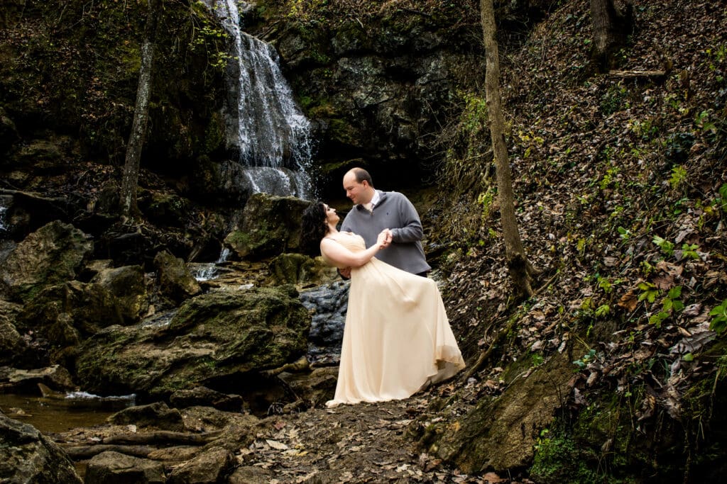 Couple standing in front of a waterfall in winter with their wedding attire on a few spots of greenery popping out in a sea of brown.