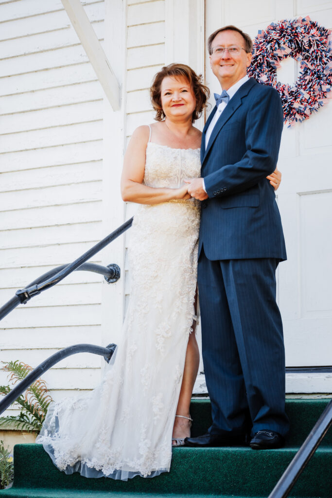 Couple eloping at a small chapel in the blue ridge mountains standing outside the white chapel with lush green landscape.