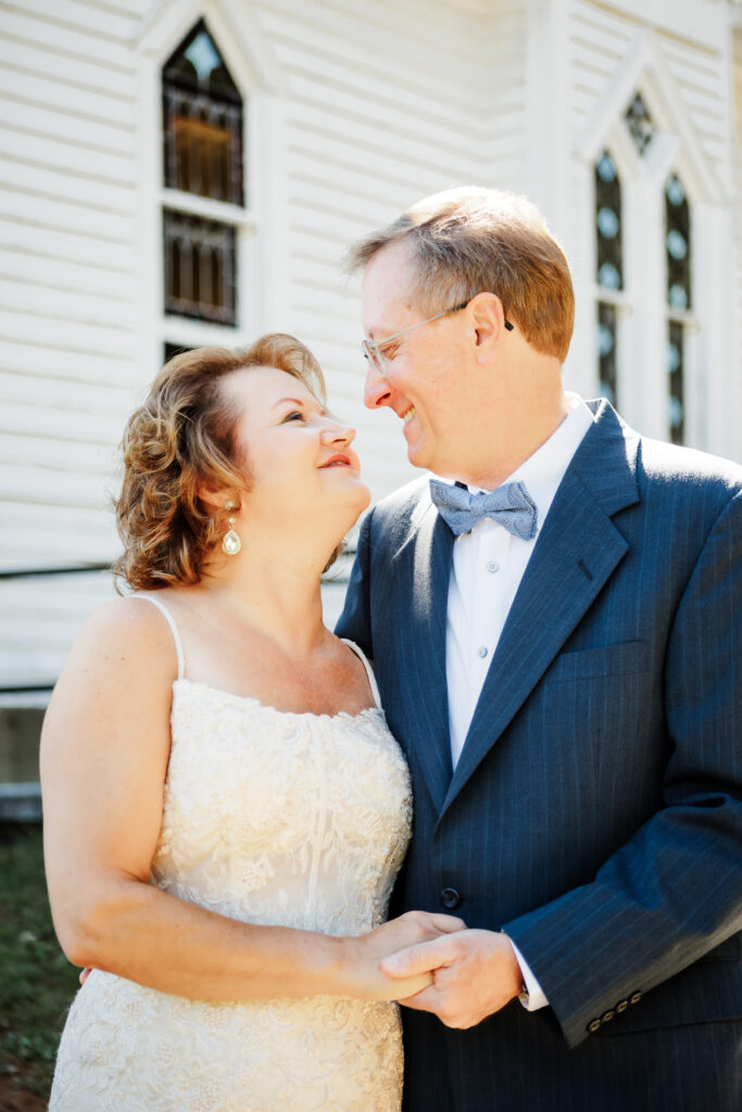 Couple eloping at a small chapel in the blue ridge mountains standing outside the white chapel with lush green landscape.
