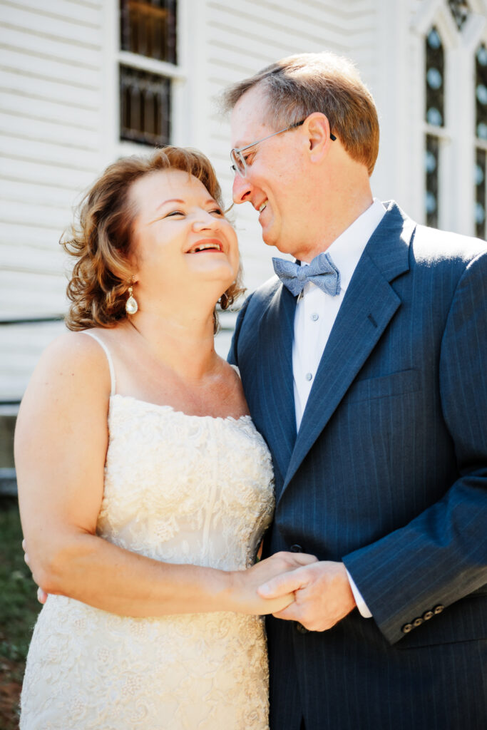 Couple eloping at a small chapel in the blue ridge mountains standing outside the white chapel with lush green landscape.