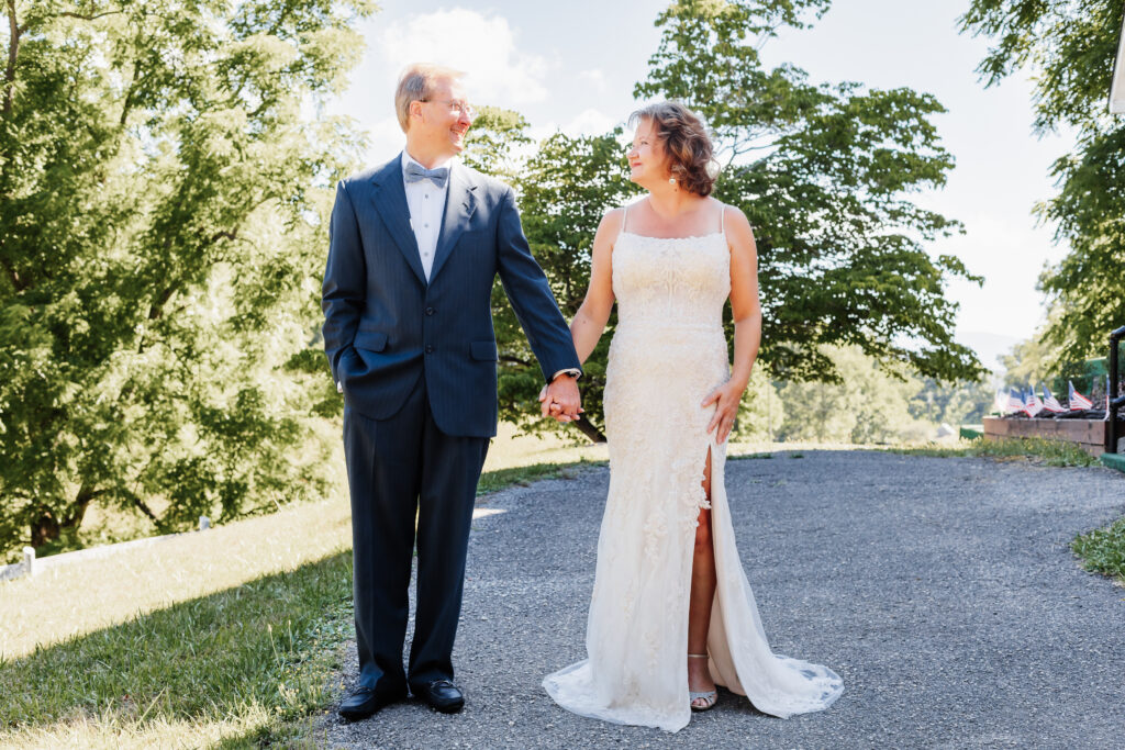 Couple eloping at a small chapel in the blue ridge mountains standing outside the white chapel with lush green landscape.