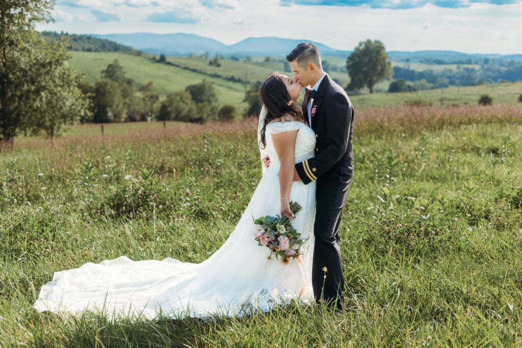 Couple getting eloping in a field with trees all green and blue rolling mountains in the distance.