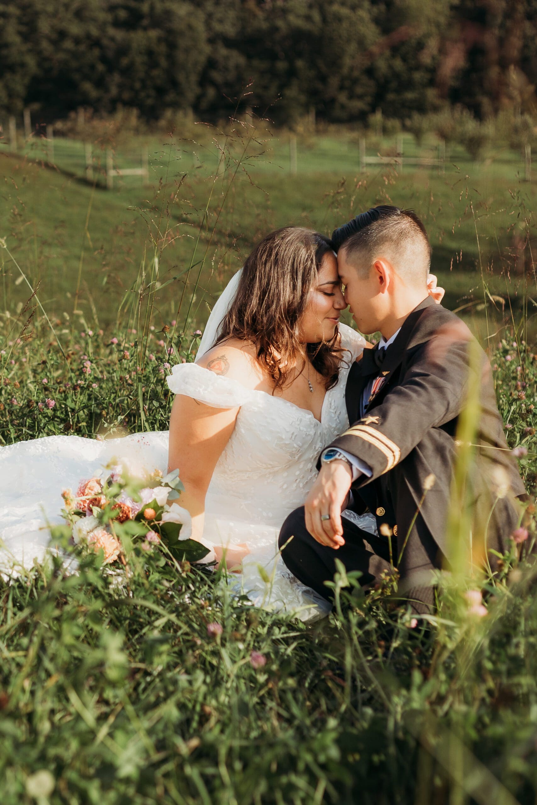 Couple in wedding attire eloping in a field of flowers surrounded by greenery. They are sitting in the grass and flowers kissing.
