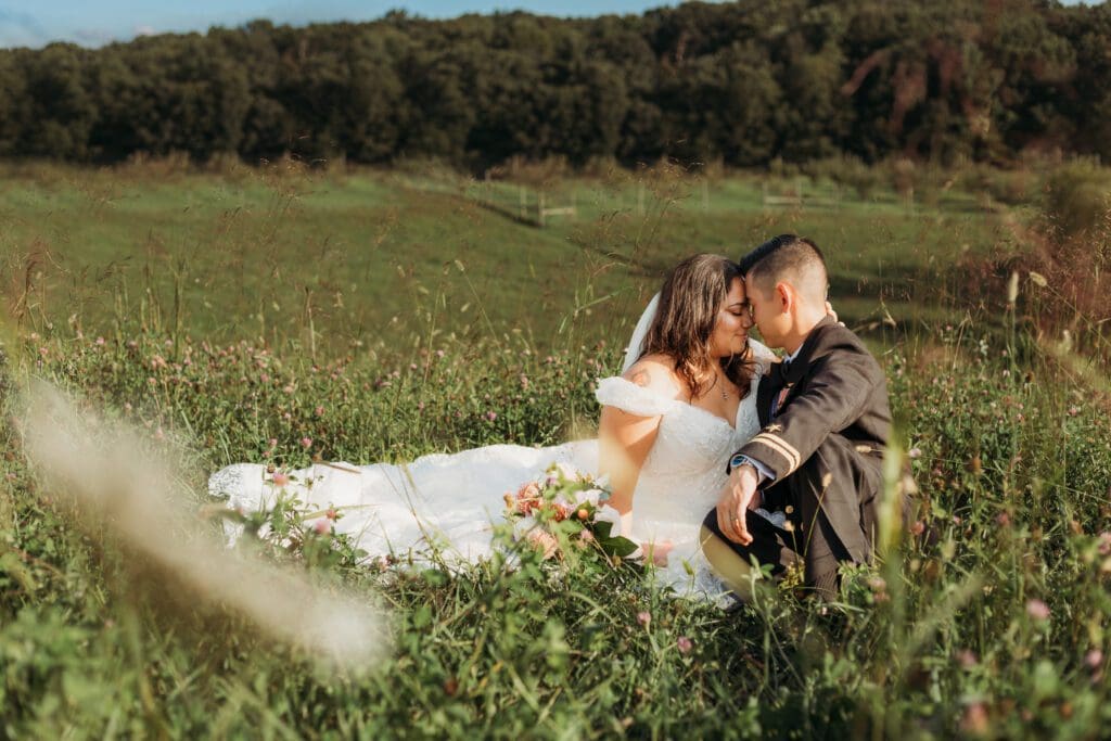 Couple in wedding attire eloping in a field of flowers surrounded by greenery. They are sitting in the grass and flowers kissing.