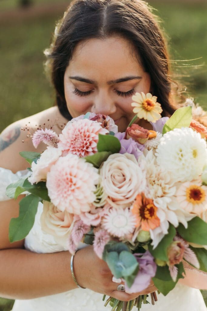Bride standing with her wedding dress all splayed out on display. She is standing in a sea of green with blue skies and blue rolling mountains in the distance.