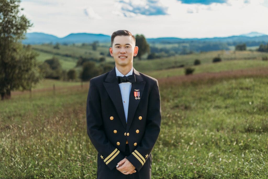 Groom is standing in a sea of green with blue skies and blue rolling mountains in the distance.