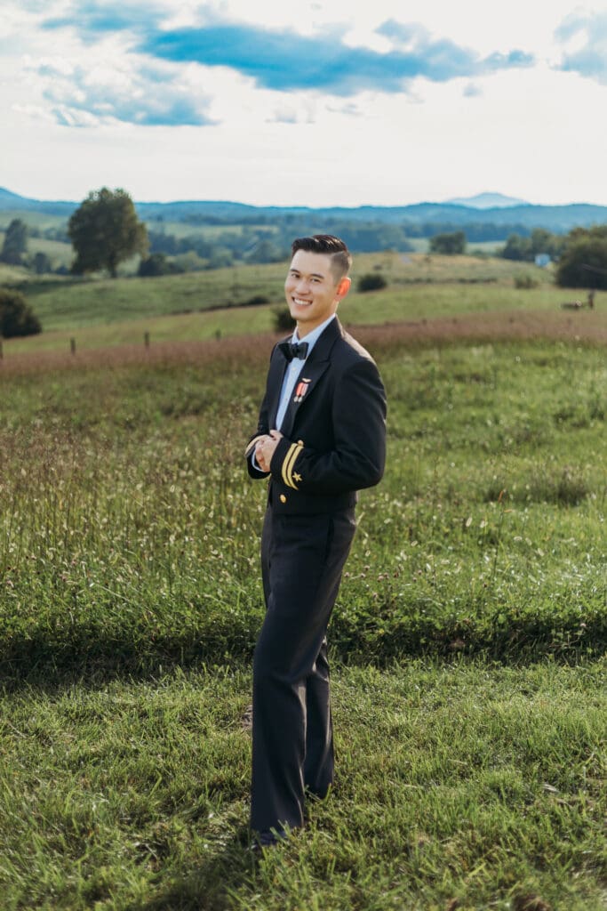 Groom is standing in a sea of green with blue skies and blue rolling mountains in the distance.
