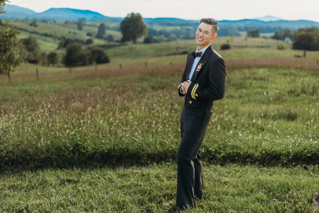Groom is standing in a sea of green with blue skies and blue rolling mountains in the distance.