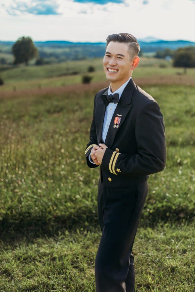 Groom is standing in a sea of green with blue skies and blue rolling mountains in the distance.