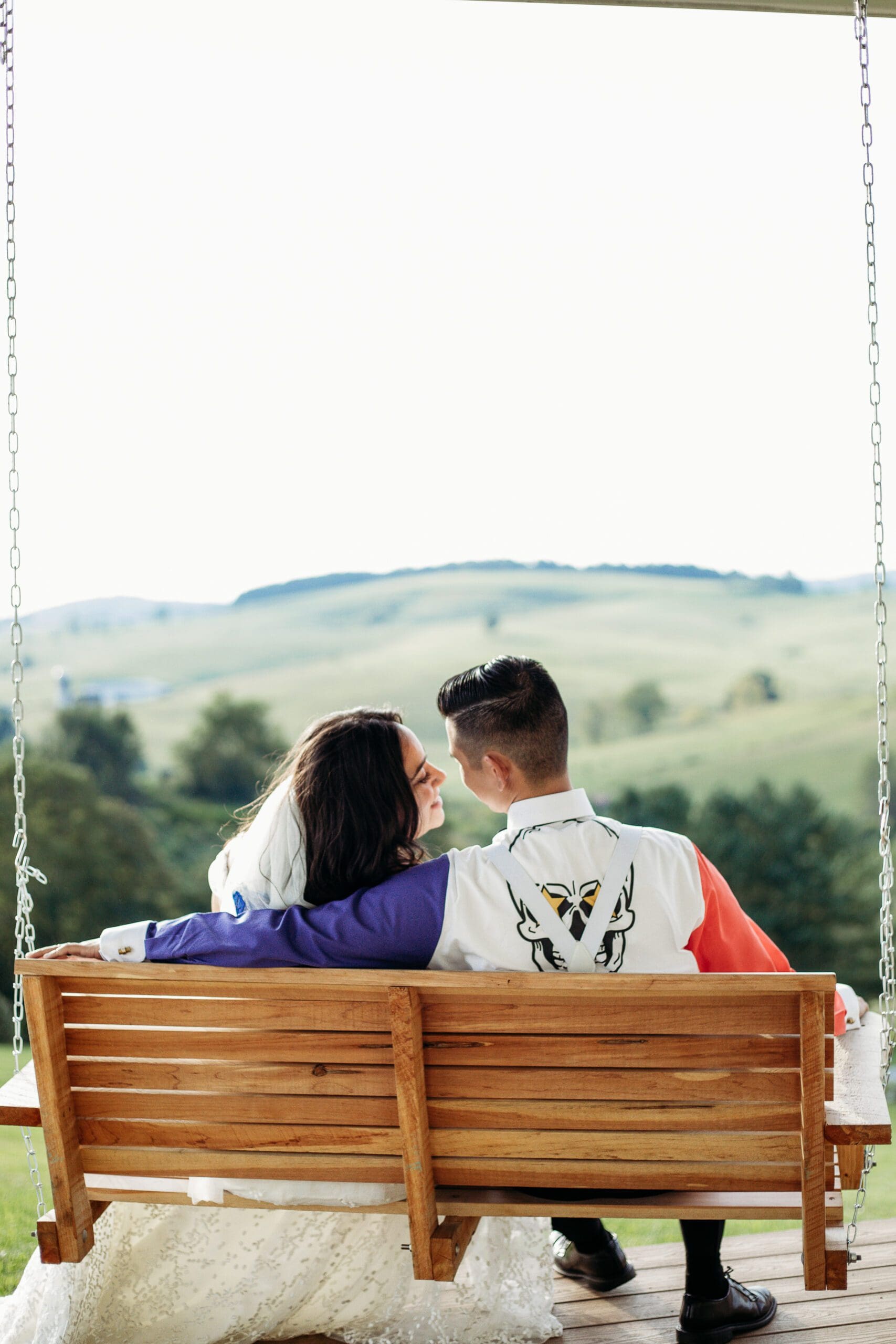 Couple just married sitting on a porch swing with mountains in the distance.