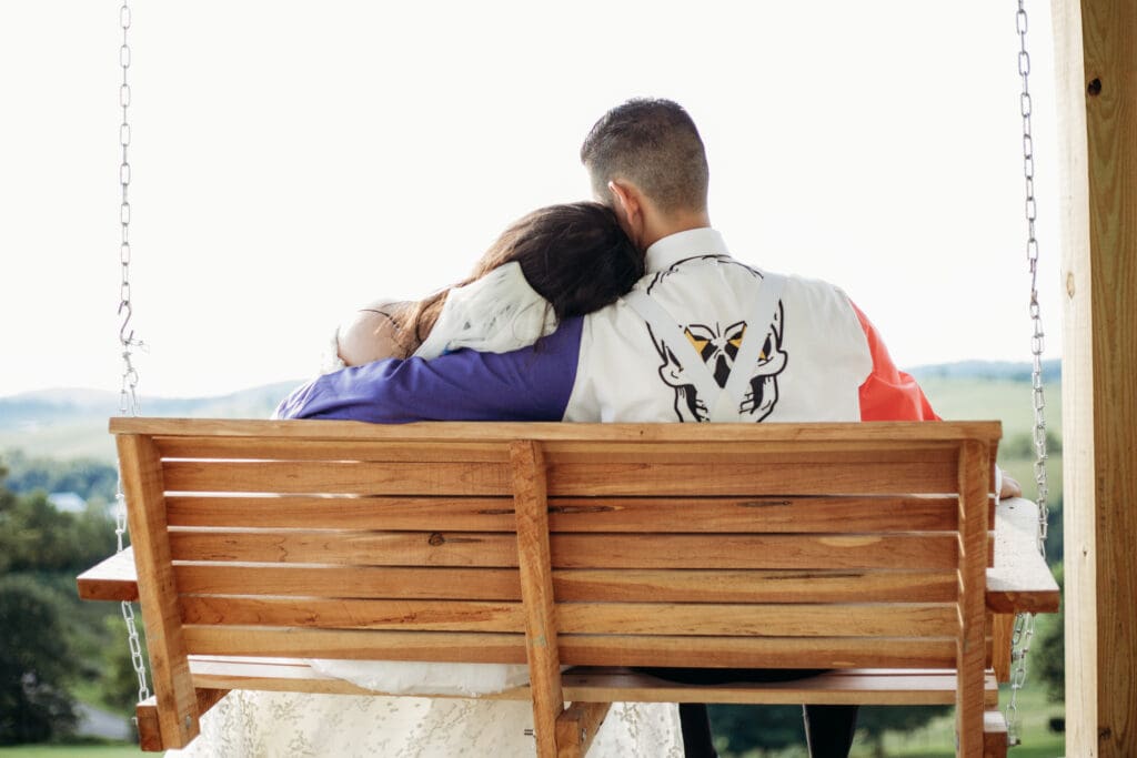Couple just married sitting on a porch swing with mountains in the distance.