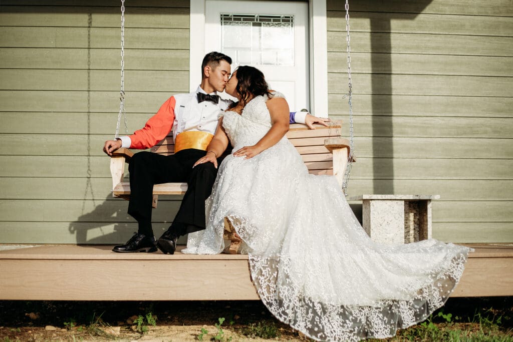 Couple just married sitting on a porch swing with mountains in the distance.