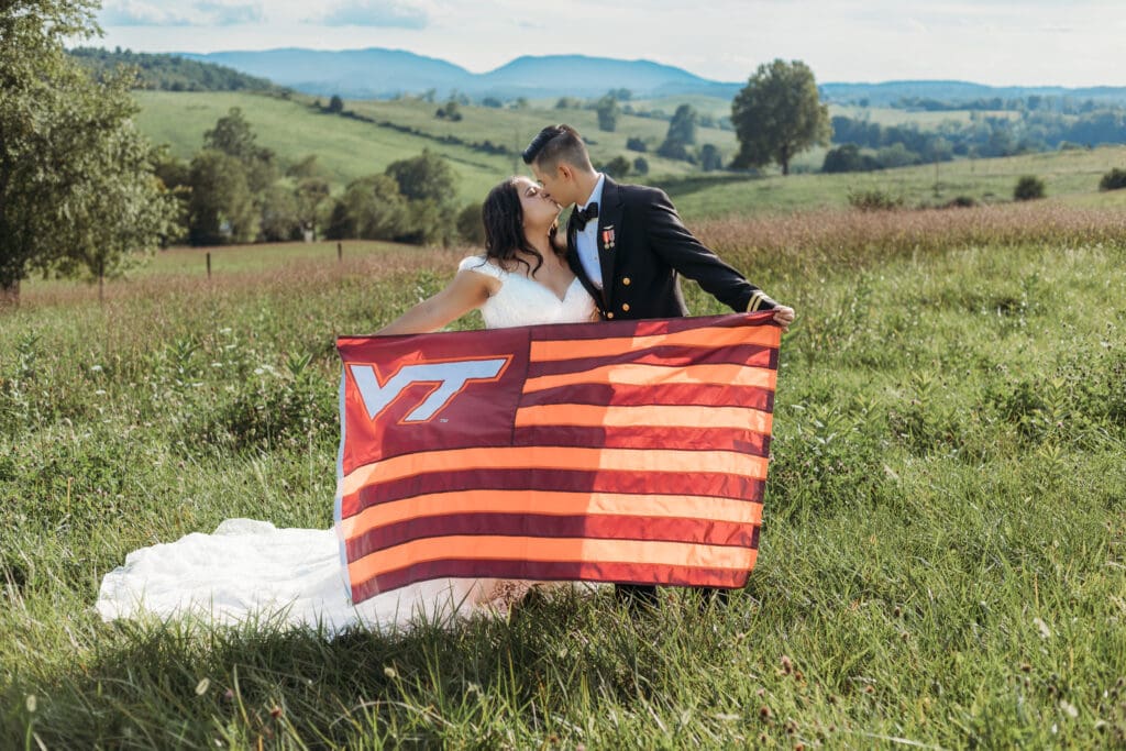 Couple getting eloping in a field with trees all green and blue rolling mountains in the distance. Holding VT flag.