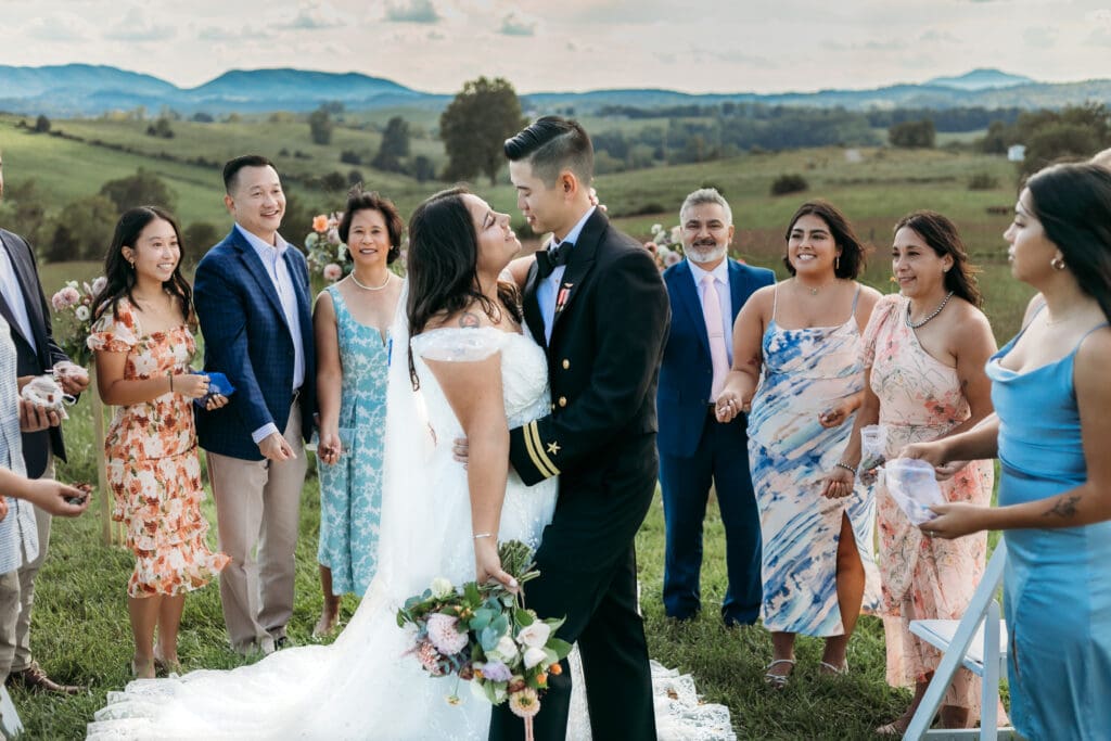 A mountain elopement where the bridse and groom are kissing with the family standing around them throwing rose petals and looking on with adoration.