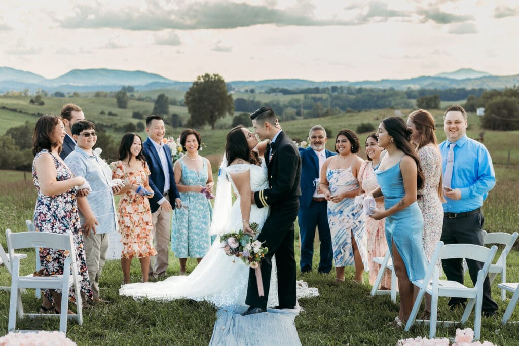 A mountain elopement where the bridse and groom are kissing with the family standing around them throwing rose petals and looking on with adoration.