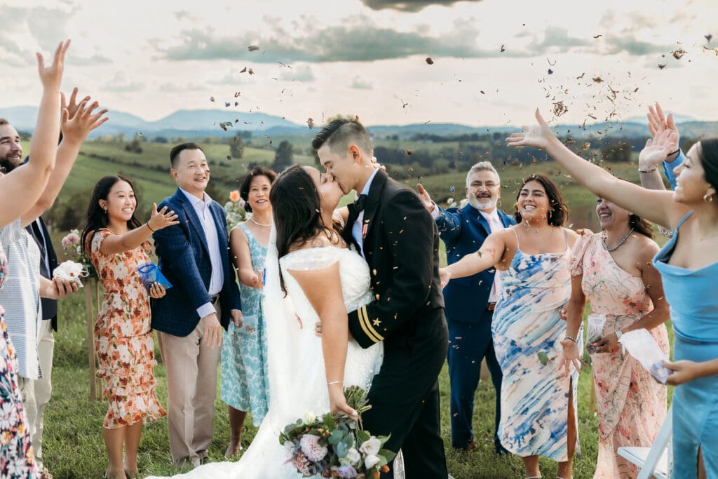 A mountain elopement where the bridse and groom are kissing with the family standing around them throwing rose petals and looking on with adoration.