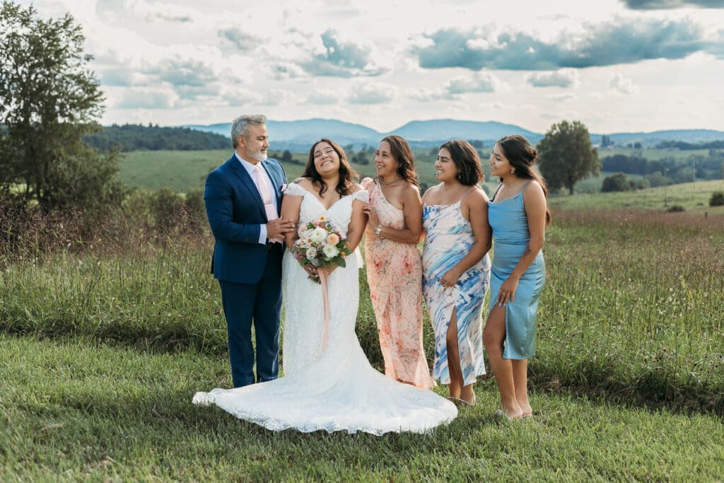 A bride surrounded by family fawning over her in a field of green with rolling green mountains in the background.
