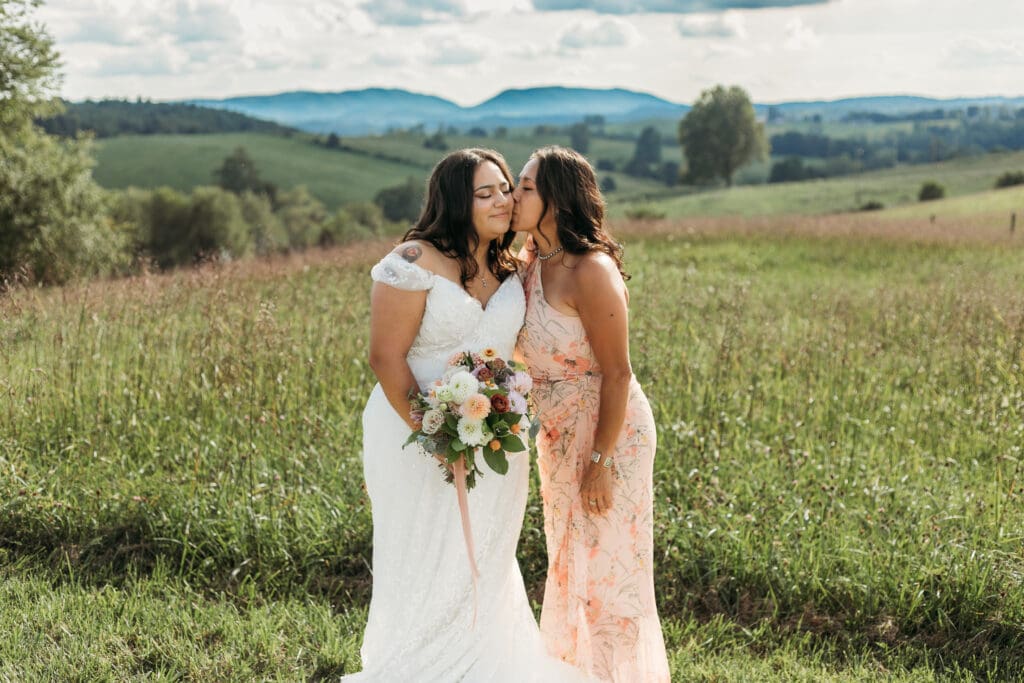 A bride with mom fawning over her in a field of green with rolling green mountains in the background.