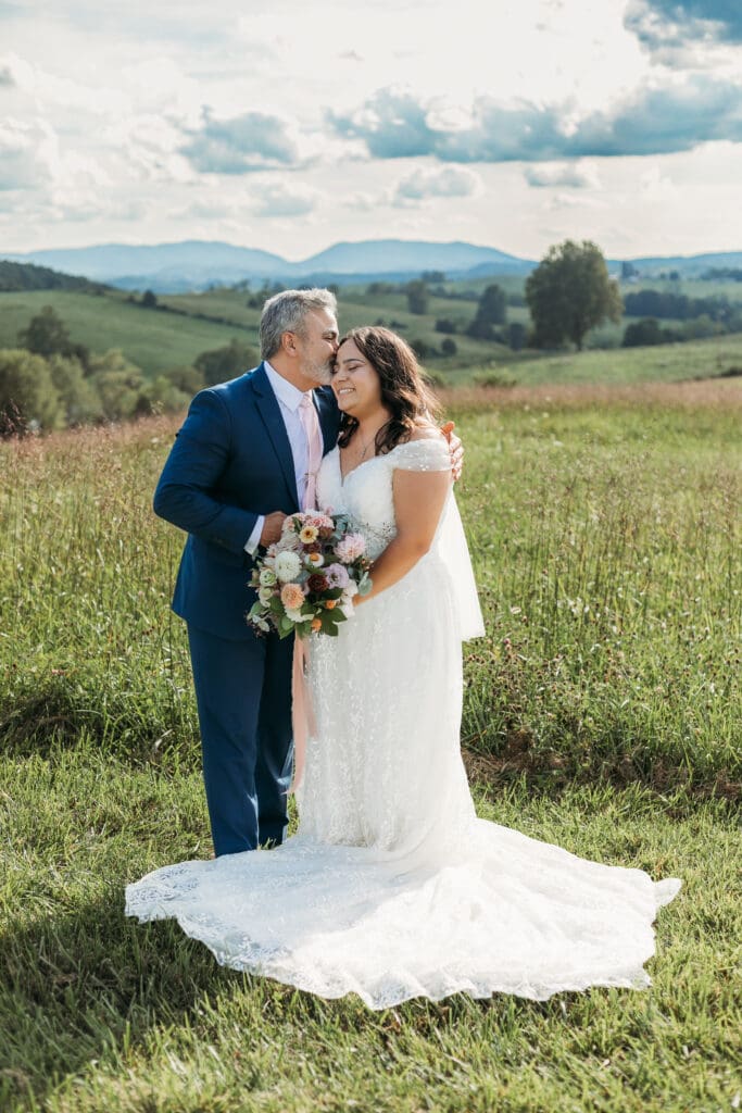 A bride with dad fawning over her in a field of green with rolling green mountains in the background.