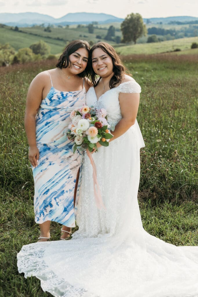 A bride with sisters fawning over her in a field of green with rolling green mountains in the background.