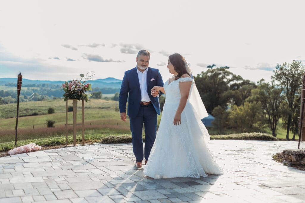 Bride having a parent dance with father at mountain elopement. They are dancing on a concrete porch with fields of green surrounding them and rolling blue mountains in the distance.