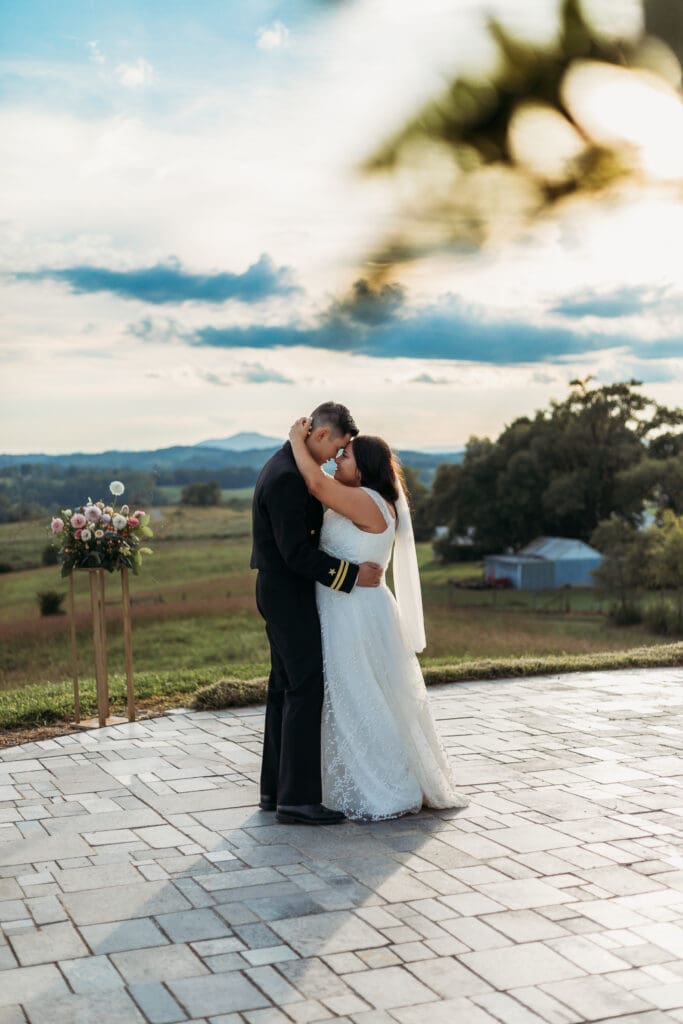 Bride and groom having a first dance at their mountain elopement. They are dancing on a concrete porch with fields of green surrounding them and rolling blue mountains in the distance.