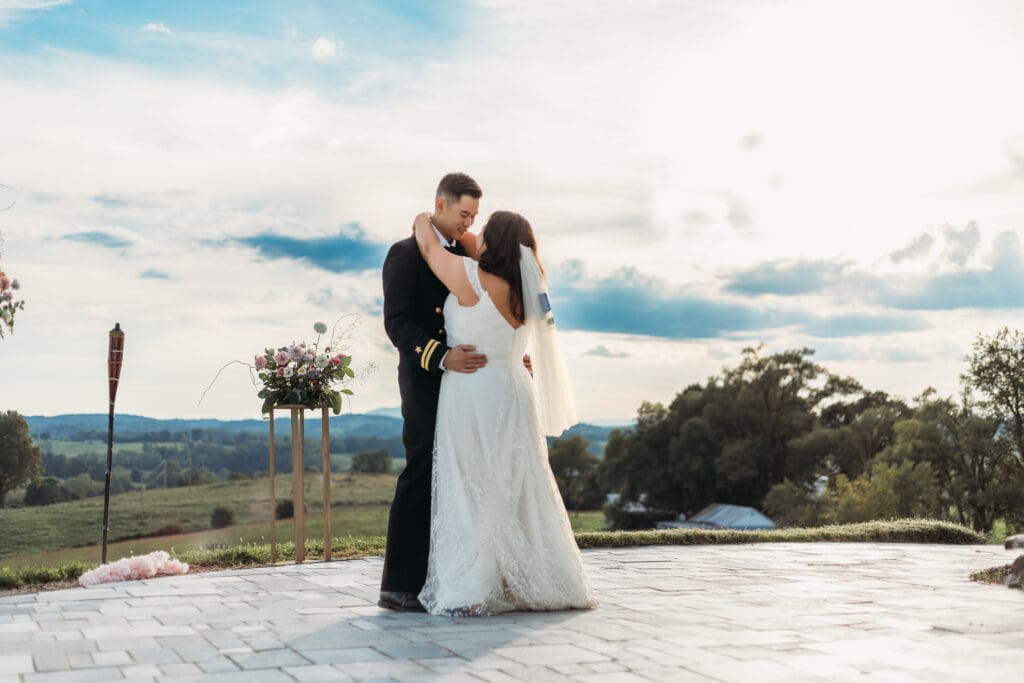 Bride and groom having a first dance at their mountain elopement. They are dancing on a concrete porch with fields of green surrounding them and rolling blue mountains in the distance.