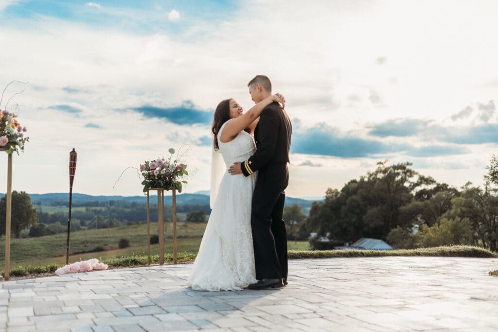 Bride and groom having a first dance at their mountain elopement. They are dancing on a concrete porch with fields of green surrounding them and rolling blue mountains in the distance.