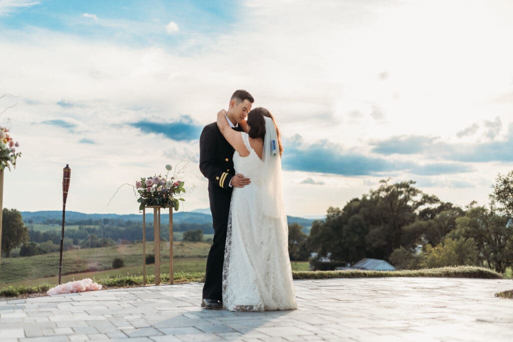 Bride and groom having a first dance at their mountain elopement. They are dancing on a concrete porch with fields of green surrounding them and rolling blue mountains in the distance.