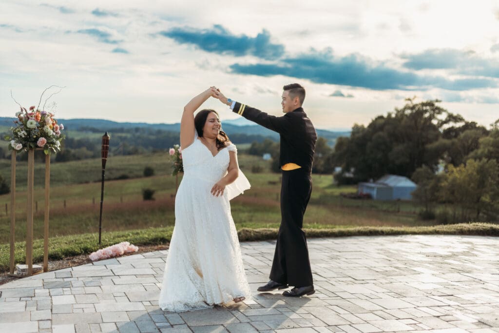 Bride and groom having a first dance at their mountain elopement. They are dancing on a concrete porch with fields of green surrounding them and rolling blue mountains in the distance.