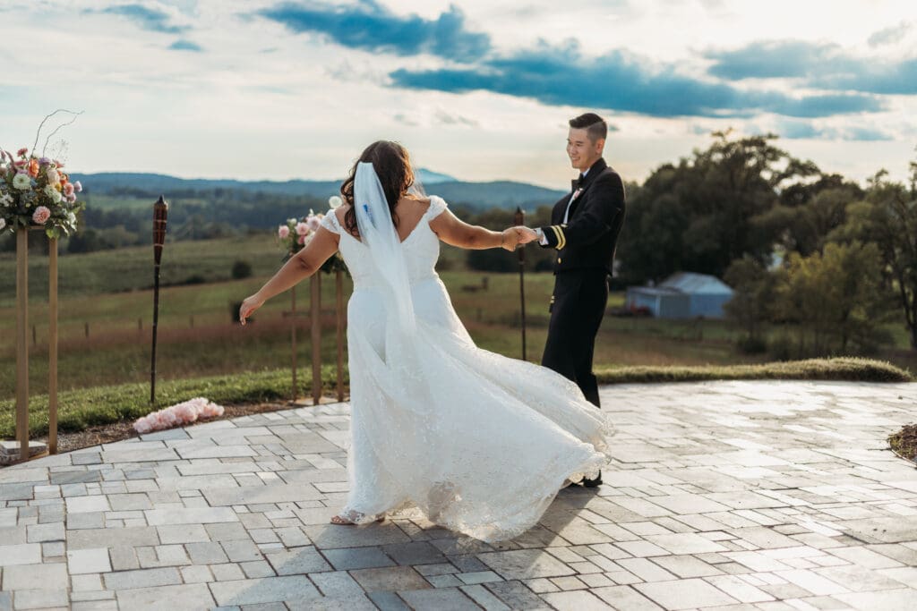 Bride and groom having a first dance at their mountain elopement. They are dancing on a concrete porch with fields of green surrounding them and rolling blue mountains in the distance.