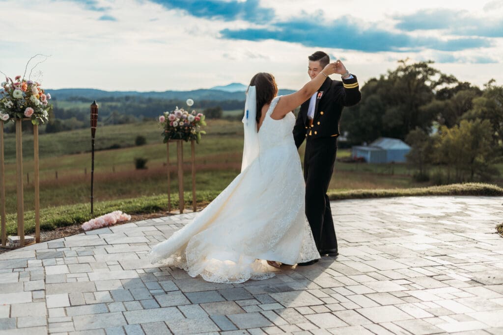 Bride and groom having a first dance at their mountain elopement. They are dancing on a concrete porch with fields of green surrounding them and rolling blue mountains in the distance.
