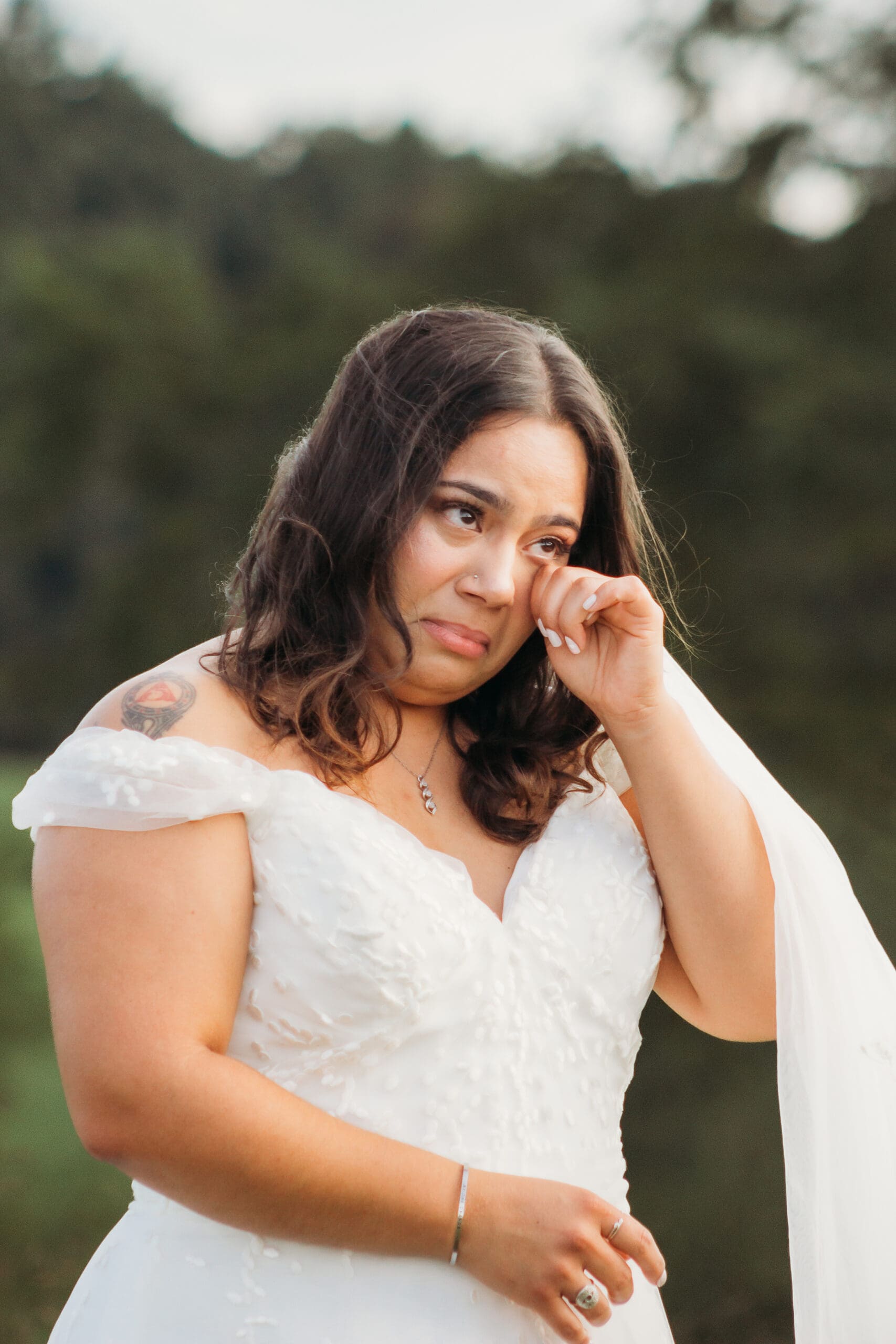 Bride and Groom being married by family member in a field of green with blue rolling mountains in the background. They have a semi circle of flower pedestals around them.