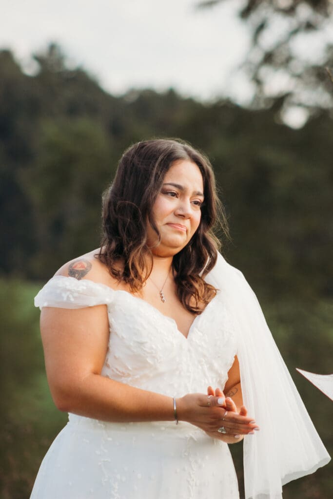 Bride and Groom being married by family member in a field of green with blue rolling mountains in the background. They have a semi circle of flower pedestals around them.