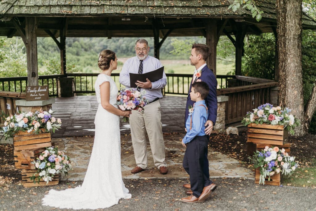 Couple getting married under gazebo eloping in front of the mountains with their son.