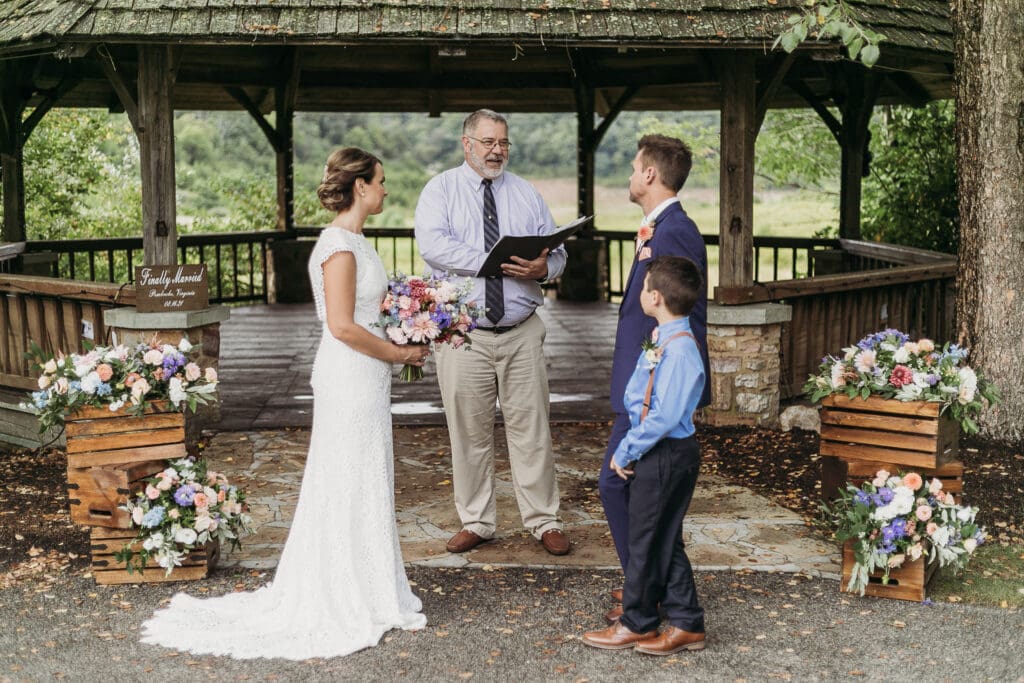 Couple getting married under gazebo eloping in front of the mountains with their son.